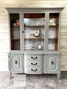 an antique china cabinet with glass doors and drawers, painted in light gray color scheme