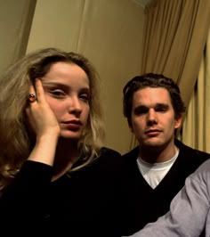 a man and woman sitting next to each other in front of a curtained window