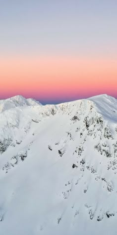 the mountains are covered in snow as the sun is setting over them and pink sky