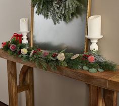 a wooden table topped with candles and greenery next to a framed photo on the wall