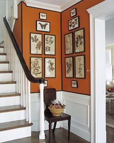 an orange wall with pictures on it and a chair in the corner next to some stairs