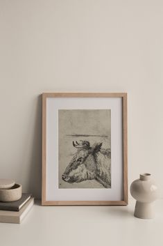 an animal is sitting on a shelf next to a white vase and a framed photograph