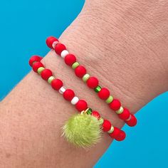 two red bracelets with green beads and a pom - pom on the wrist