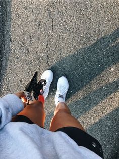 a person with their feet on the ground wearing white and black shoes, while holding onto a skateboard