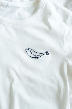 a white t - shirt with an embroidered whale on it