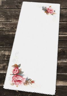 a white table cloth with pink roses on it and wooden planks in the background