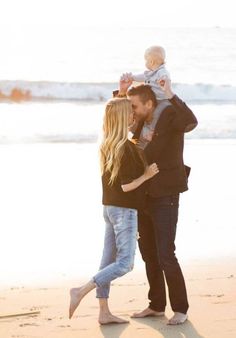 a man and woman holding a baby on the beach while standing next to each other