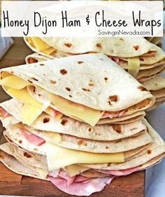 a stack of tortillas with ham and cheese wrapped in wrappers on a cutting board