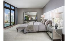 a bedroom with a large bed, mirrored nightstands and windows overlooking the cityscape