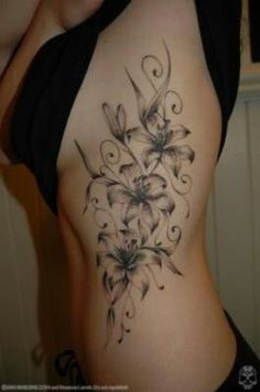 a woman's stomach with flowers and swirls tattooed on the side of her body