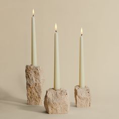 three white candles sitting on top of rocks next to each other