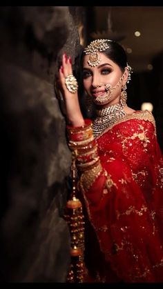 a woman in a red and gold bridal outfit holding her hand up to the side