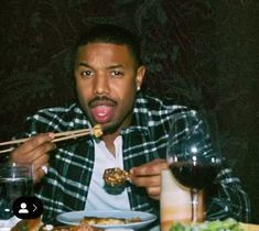 a man sitting at a table eating food with chopsticks in front of him