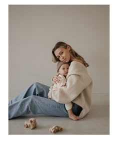 a woman sitting on the ground holding a baby in her arms and two wooden toys behind her