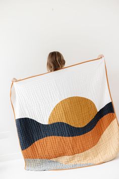 a woman is holding up a quilt with an orange and blue wave design on it