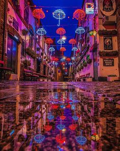 an empty street with many umbrellas hanging from it's sides and lights reflecting in the wet pavement