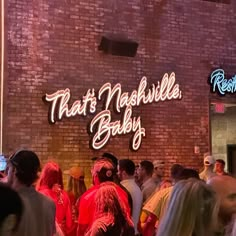 a group of people standing in front of a brick building with neon signs on it