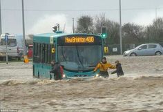 people are standing in the water near a bus that is driving through flood waters on a city street