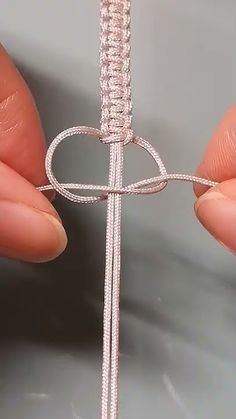 a person holding a piece of silver wire with a knot on it's end