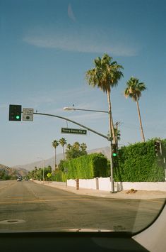 an intersection with palm trees and a street sign on the right side of the road