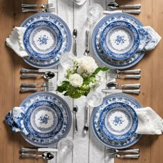 the table is set with blue and white china plates, silverware, and flowers