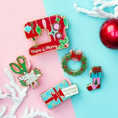 several christmas themed pins and ornaments on a pink, blue, and green background