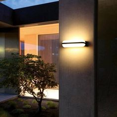 an outdoor wall light on the side of a building at night with a tree in the foreground