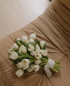 a bouquet of white tulips sitting on top of a brown couch cushiones