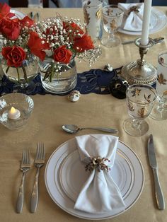 the table is set with silverware and red roses