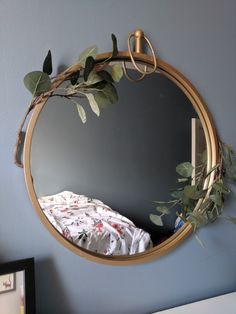 a round mirror hanging on the wall above a bed with leaves and branches in it