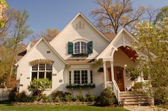 a white house with green shutters on the front and side windows, surrounded by trees