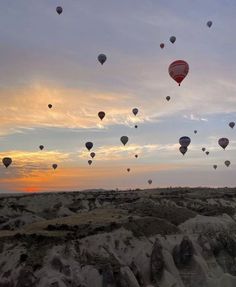 many hot air balloons are flying in the sky over some rocks and sand at sunset