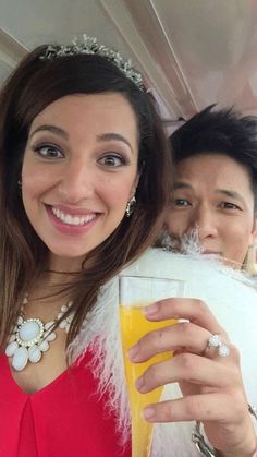 two people are posing for a photo while holding glasses with orange juice in front of them