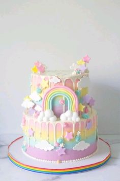 a cake decorated with pastel rainbows, clouds and stars on a white table