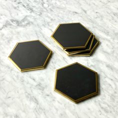 three black and gold hexagonal coasters sitting on a marble counter top,