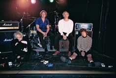 four people sitting on stage with guitars and amps