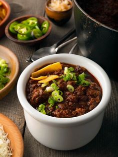 a bowl filled with chili and green onions next to other bowls full of food on a table