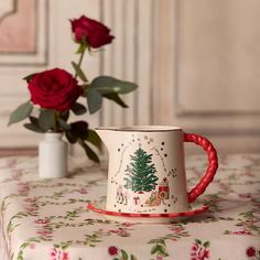 a coffee cup sitting on top of a table next to a vase filled with red roses