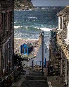 an alley way leading to the ocean with houses on either side and waves crashing into the shore