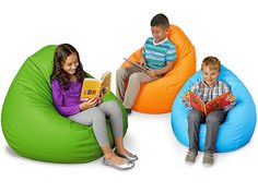 three children are sitting on bean bags reading books and talking to each other while the boy is holding a book