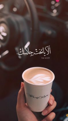 a person holding a cup of coffee in their hand with arabic writing on the screen