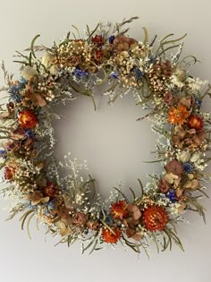 a wreath with dried flowers and foliage on the front is hung on a wall in an empty room