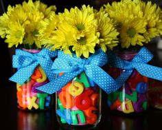 three mason jars filled with yellow flowers and colorful letters are sitting on a table next to each other