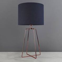 a lamp with a blue shade on it sitting on top of a white table next to a gray wall