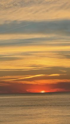 the sun is setting over the ocean with clouds in the sky