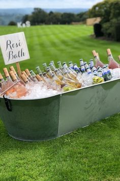 a metal tub filled with lots of bottles of wine and ice on top of a lush green field