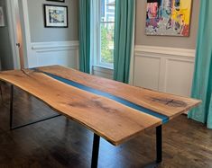 a wooden table sitting in front of a window next to a painting on the wall