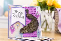 a happy birthday card with a peacock on the front, and a purple envelope in the back