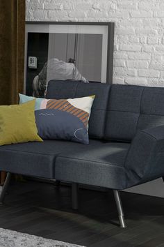 a gray couch with colorful pillows in front of a white brick wall and wooden floor