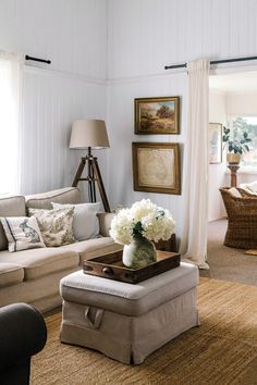 a living room filled with furniture and flowers on top of a coffee table in front of a window